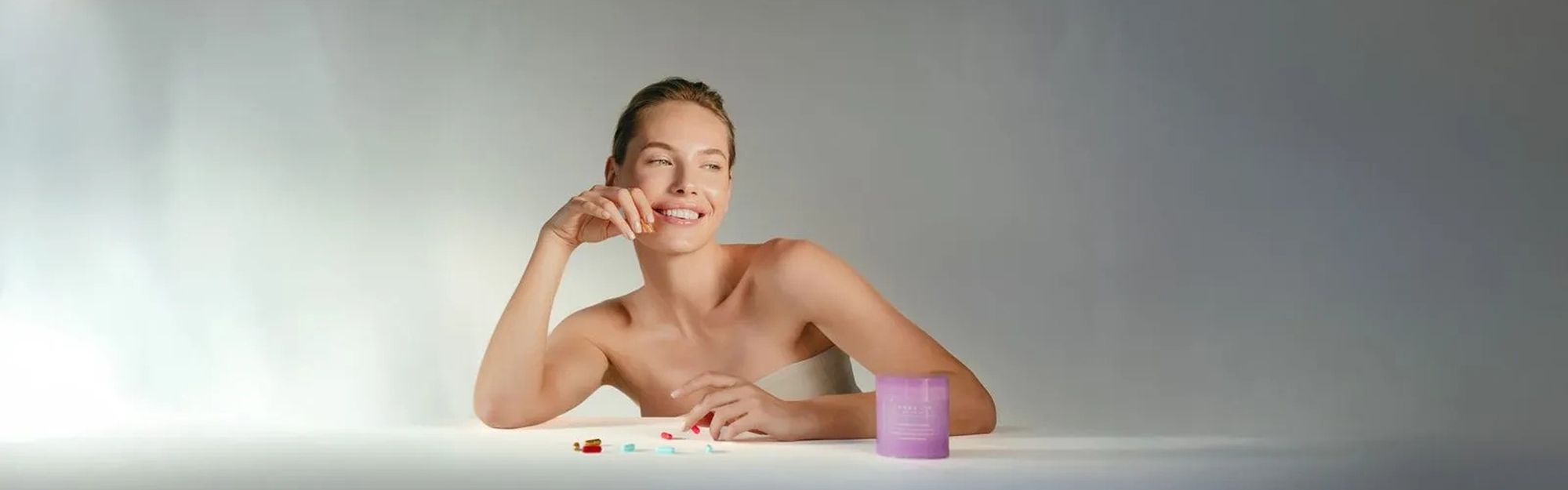 A woman sits at a table with longevity vitamins and a Longevity Method supplement jar