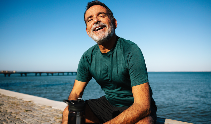 A vibrant older man laughs outdoors on a bright, sunny day near the coast, illustrating an active lifestyle and cellular health benefits